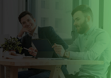 Two men collaborate at a table with a laptop, discussing digital marketing strategies and web design services.